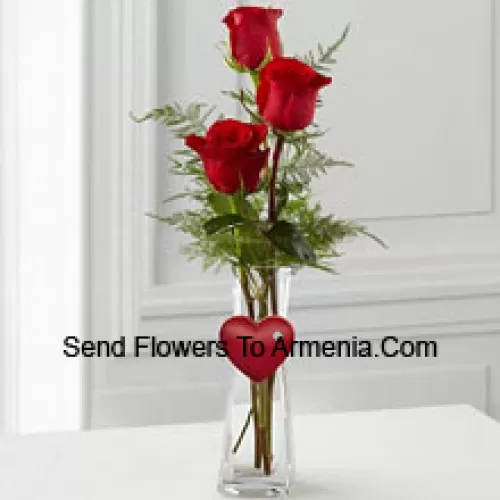 3 Red Roses In A Glass Vase Having A Small Heart Attached To It